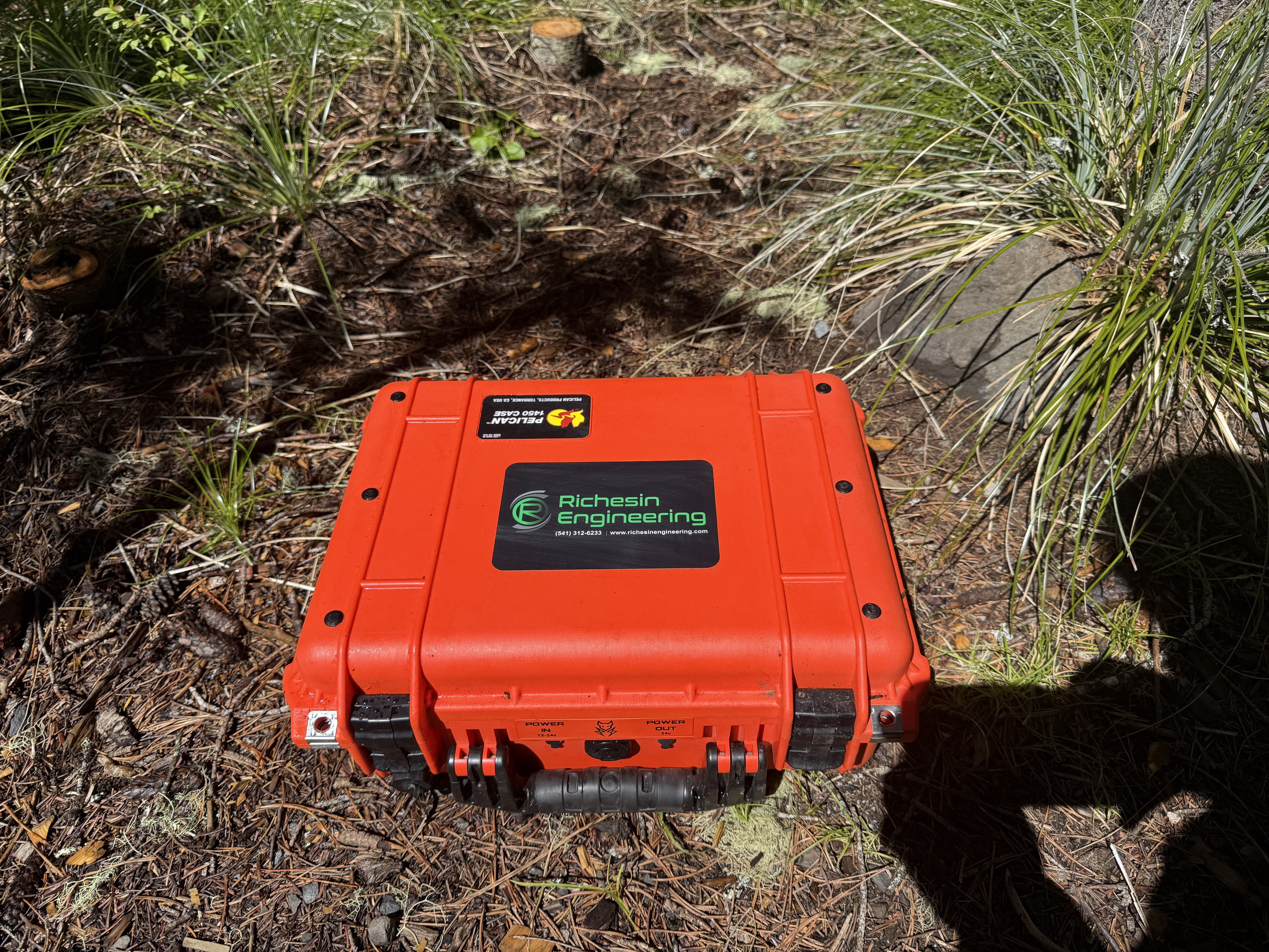 Rugged orange Pelican case with Richesin Engineering branding housing a Starlink Mini satellite internet kit, deployed on a forest floor for wildland fire communications
