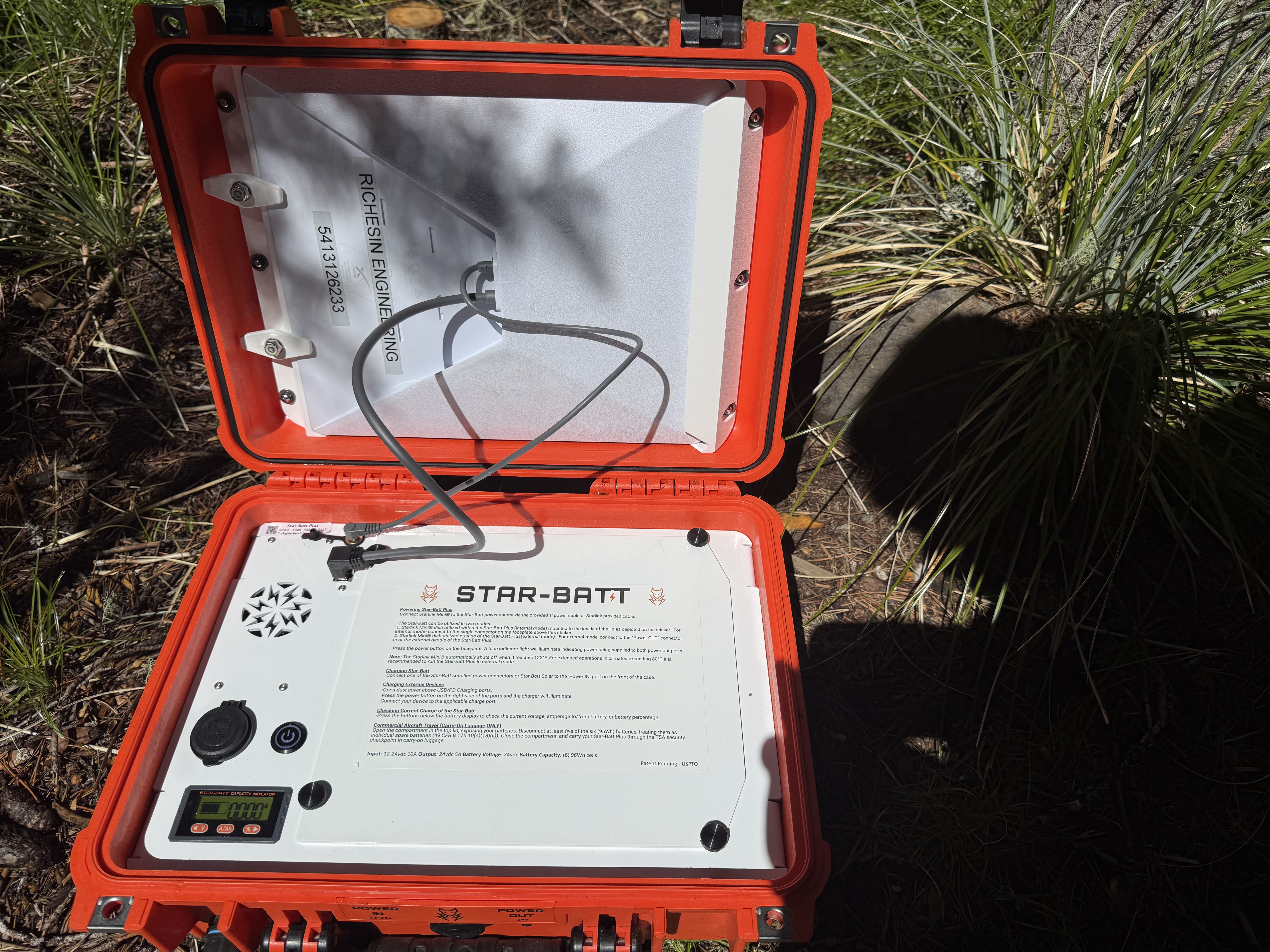 Open orange Pelican case containing a Starlink Mini satellite internet and integrated battery system deployed in a grassy wildland fire setting