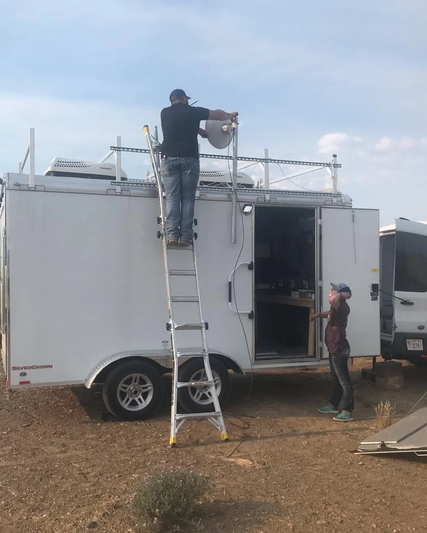 FireLine Communications technicians deploying a mobile communications trailer with satellite dish installation at a remote wildland fire incident base