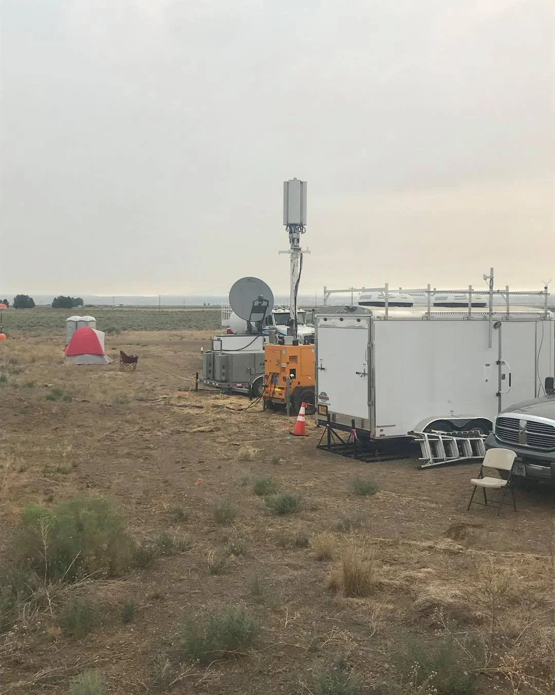 Mobile communications trailer with satellite dish, cellular antenna tower, and generator deployed at a remote wildland fire incident base camp